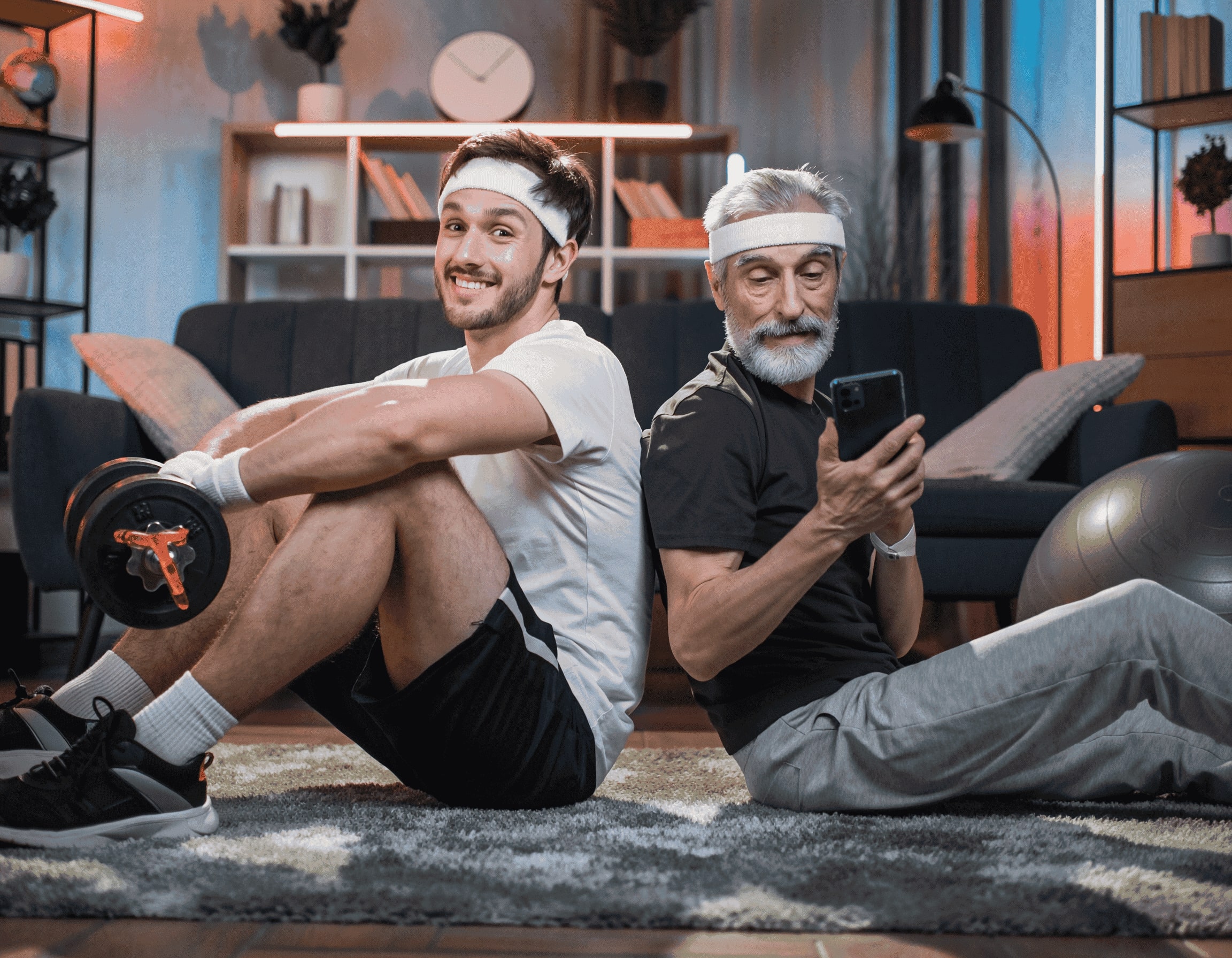 Zwei Männer beim Wohnzimmer-Workout, Rücken an Rücken, einer mit Hantel, einer mit Smartphone.